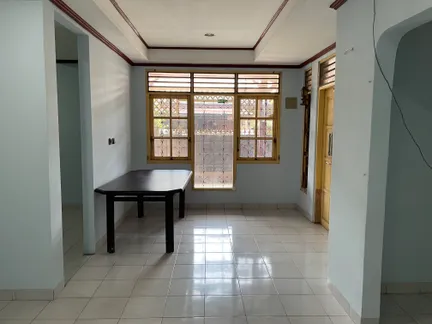 A room in an acquired house before staging: bare tiled floor, painted walls, a single dark table under a barred window, and no furnishing.